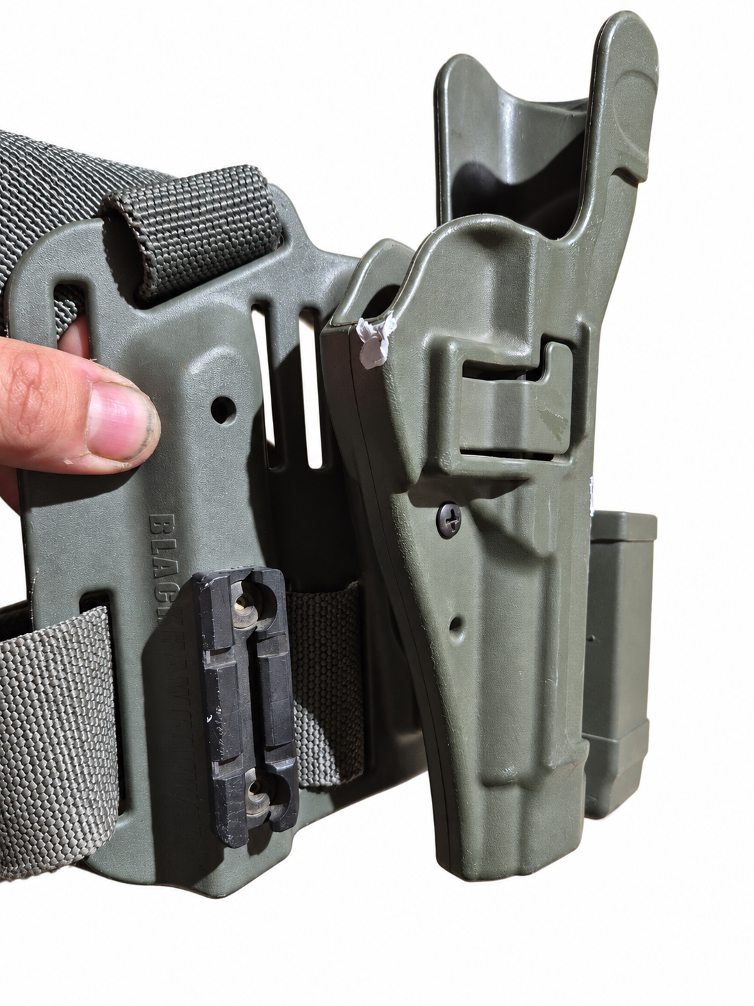 Hand-held close-up of the holster retention-button side, accessory rail and white surface marks.